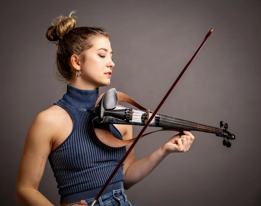 A professional violinist performing on a sleek electric violin under warm stage lights, with a small pedalboard and amp visible in the background